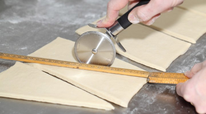 طرز تهیه کروسان - پس از بازکردن خمیر آن را به شکل مثلث برش بدهید.